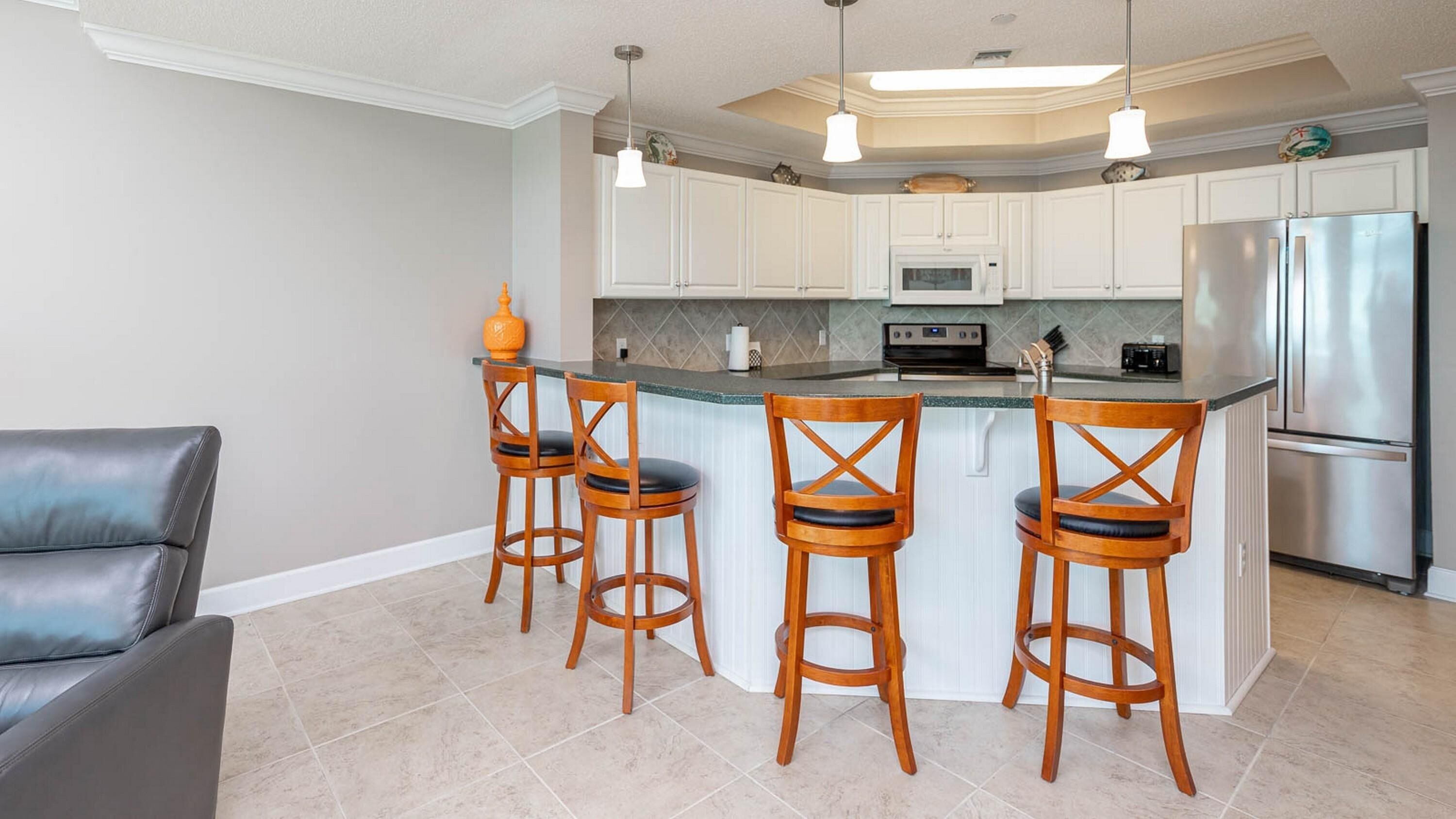 A modern kitchen with white cabinets, a stainless steel refrigerator, and a central island with bar stools.