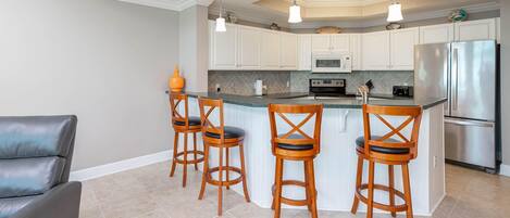A modern kitchen with white cabinets, a stainless steel refrigerator, and a central island with bar stools.