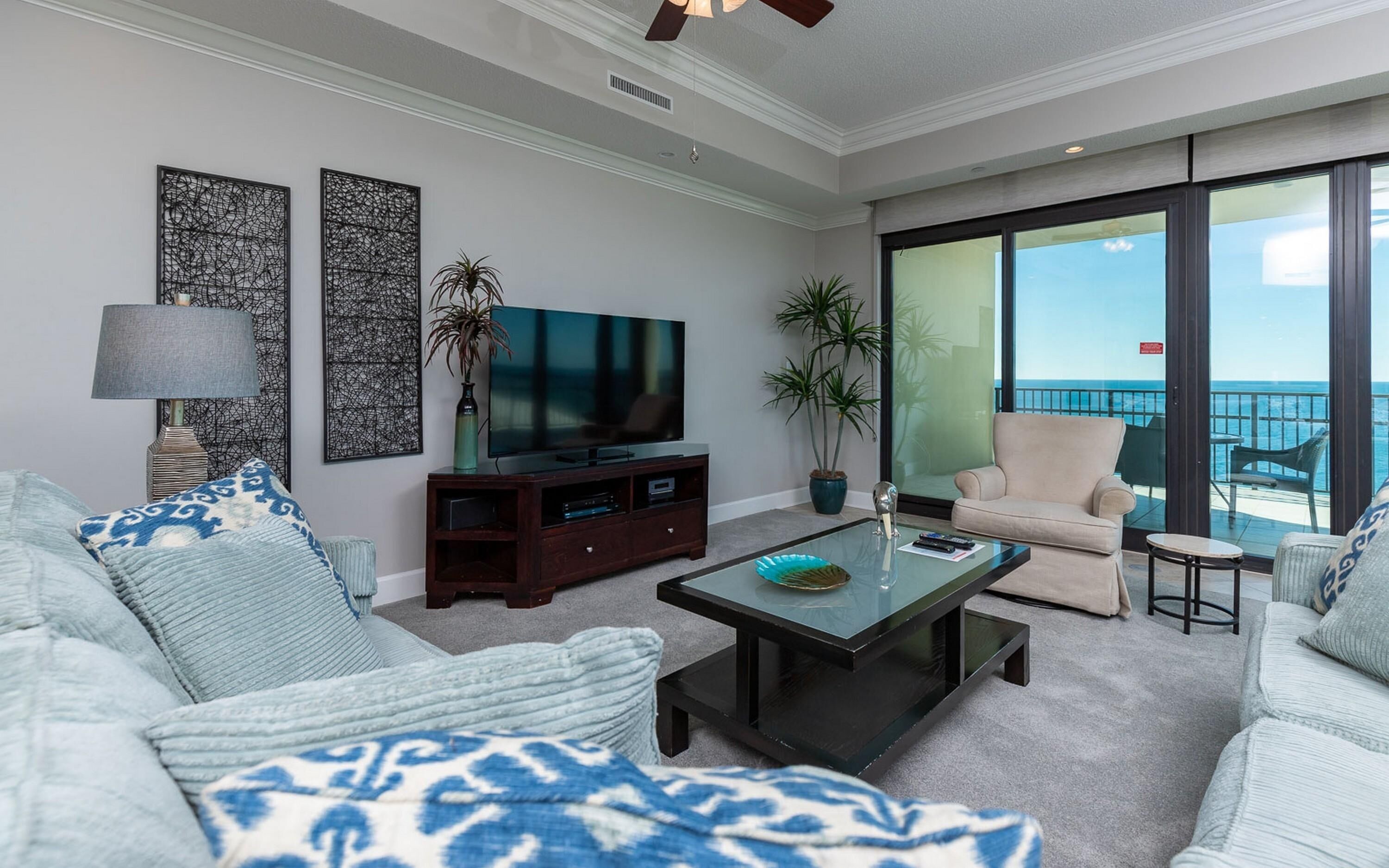 A modern living room with a sofa, coffee table, TV, and large windows overlooking the ocean.