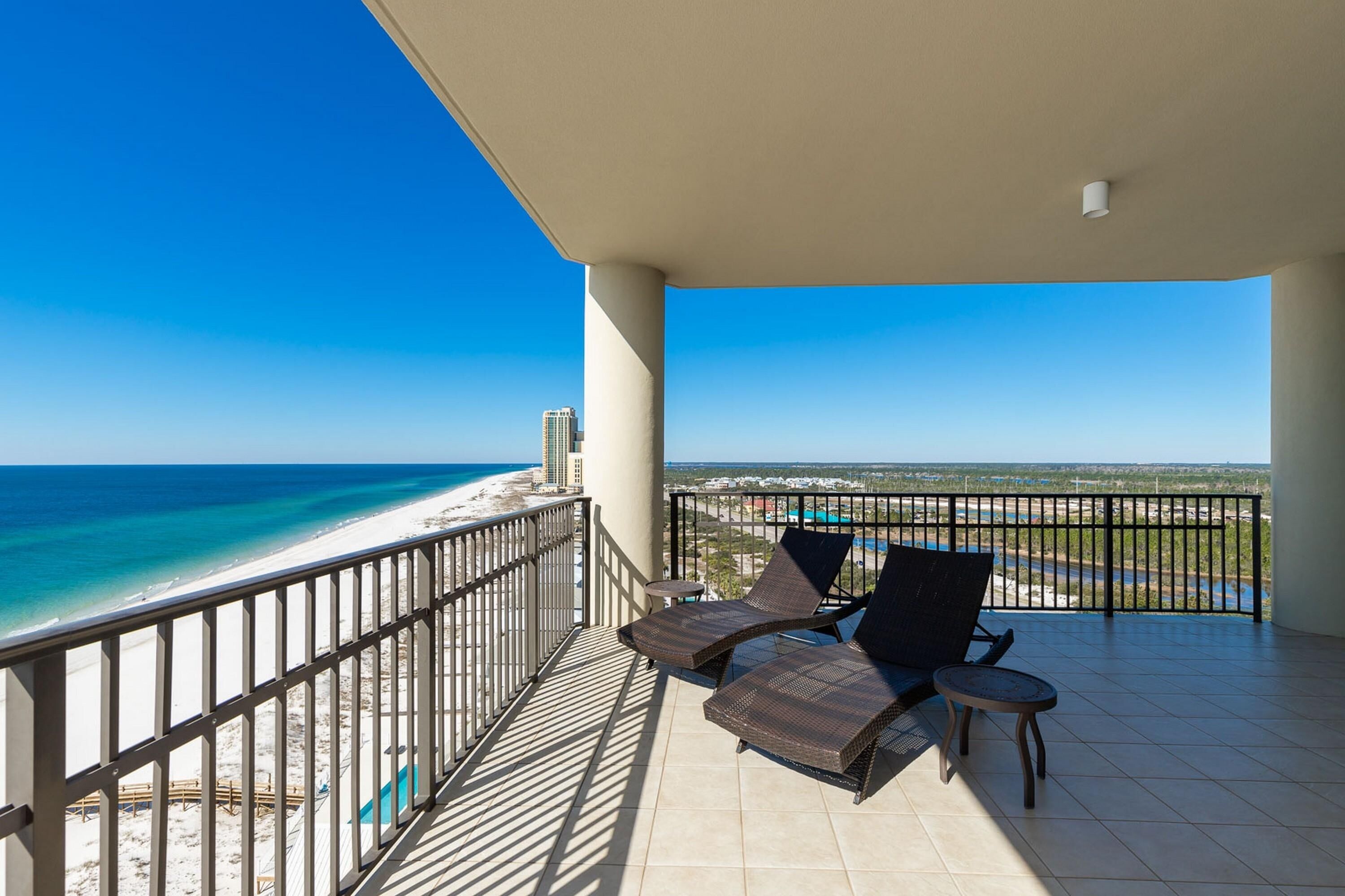 Een balkon met twee lounge stoelen en een klein tafeltje, met uitzicht op een strand en de oceaan.