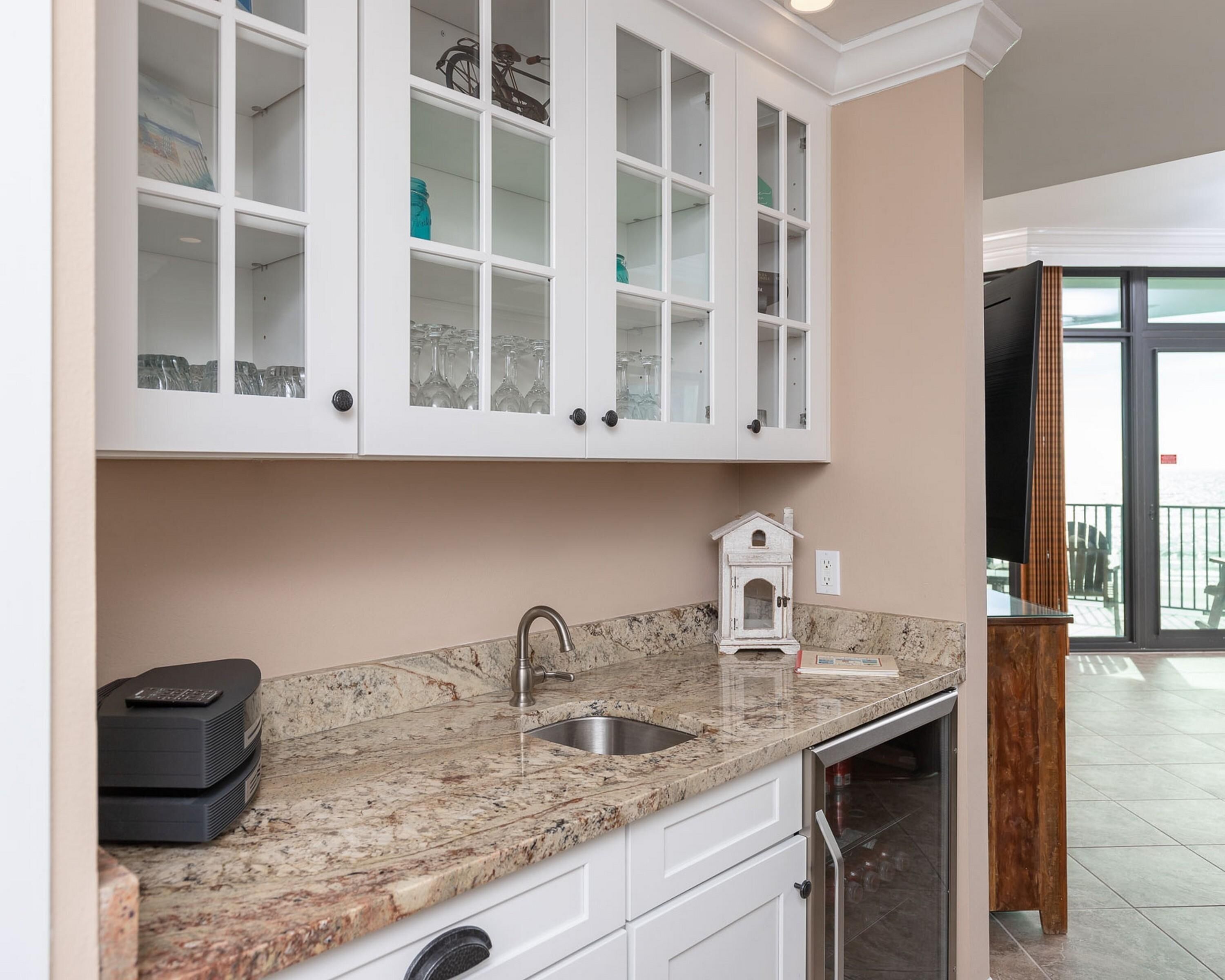 Una cocina con armarios blancos, encimera de granito y una pequeña decoración con forma de casa.