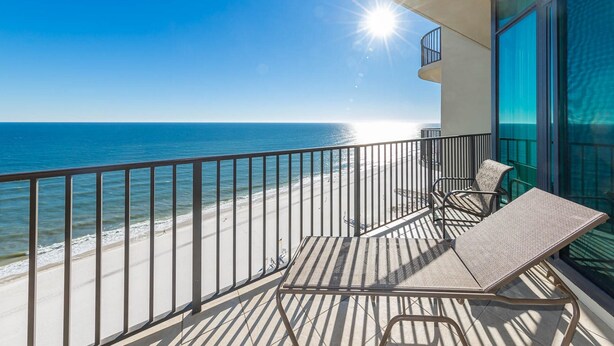 A balcony with a view of the beach and ocean, featuring a table and two chairs.