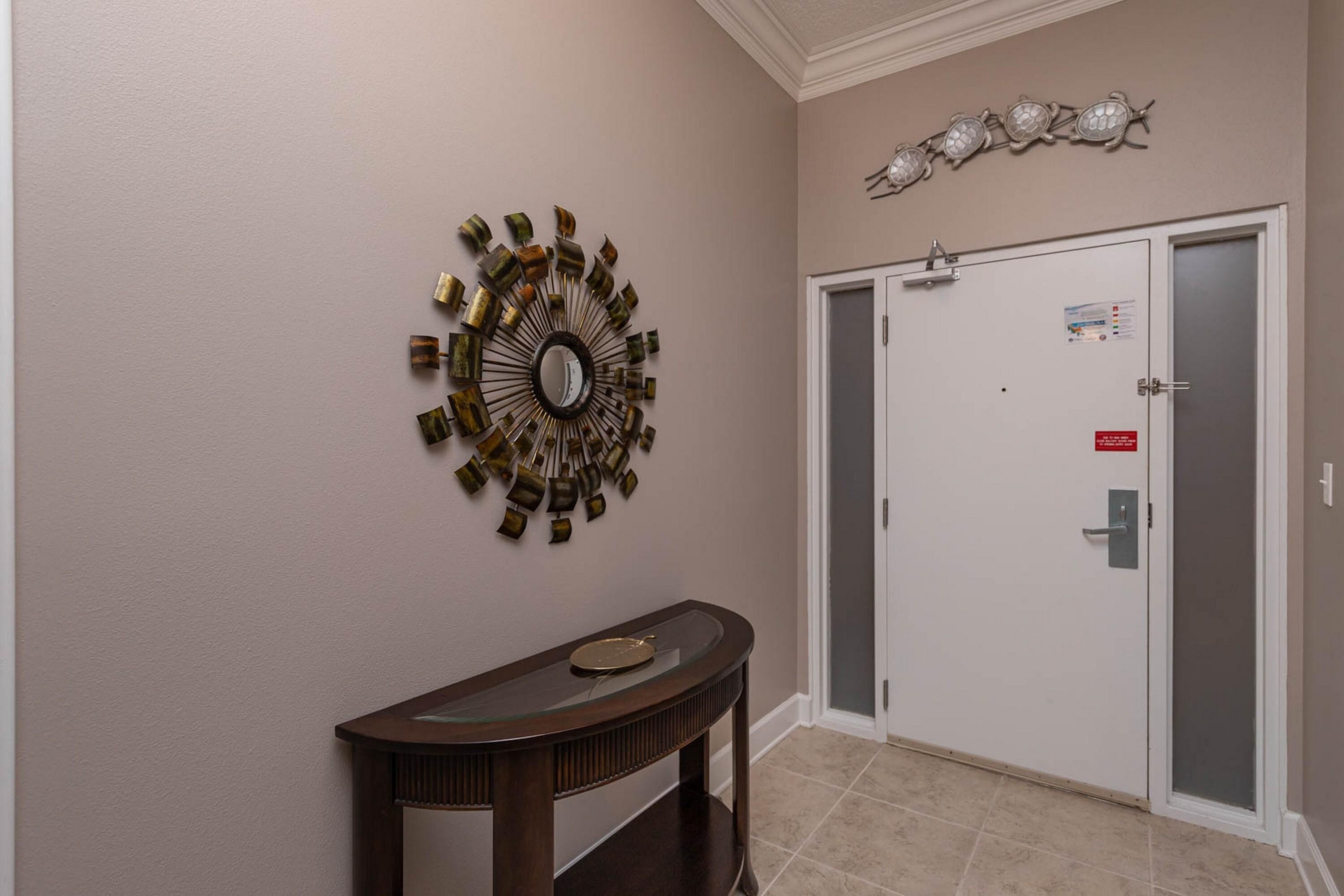 A hallway with a decorative mirror, a console table, and a door with a sign.