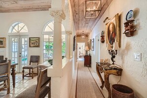 A hallway with a dining area, featuring a table and chairs, a lamp, and wall-mounted decor.