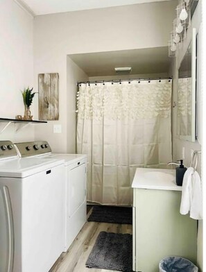 Efficient laundry facilities with a front-loading washer and dryer, sink, and shower area.