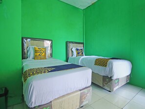Two twin beds with headboards, white bedding, and patterned throw pillows against a green wall.