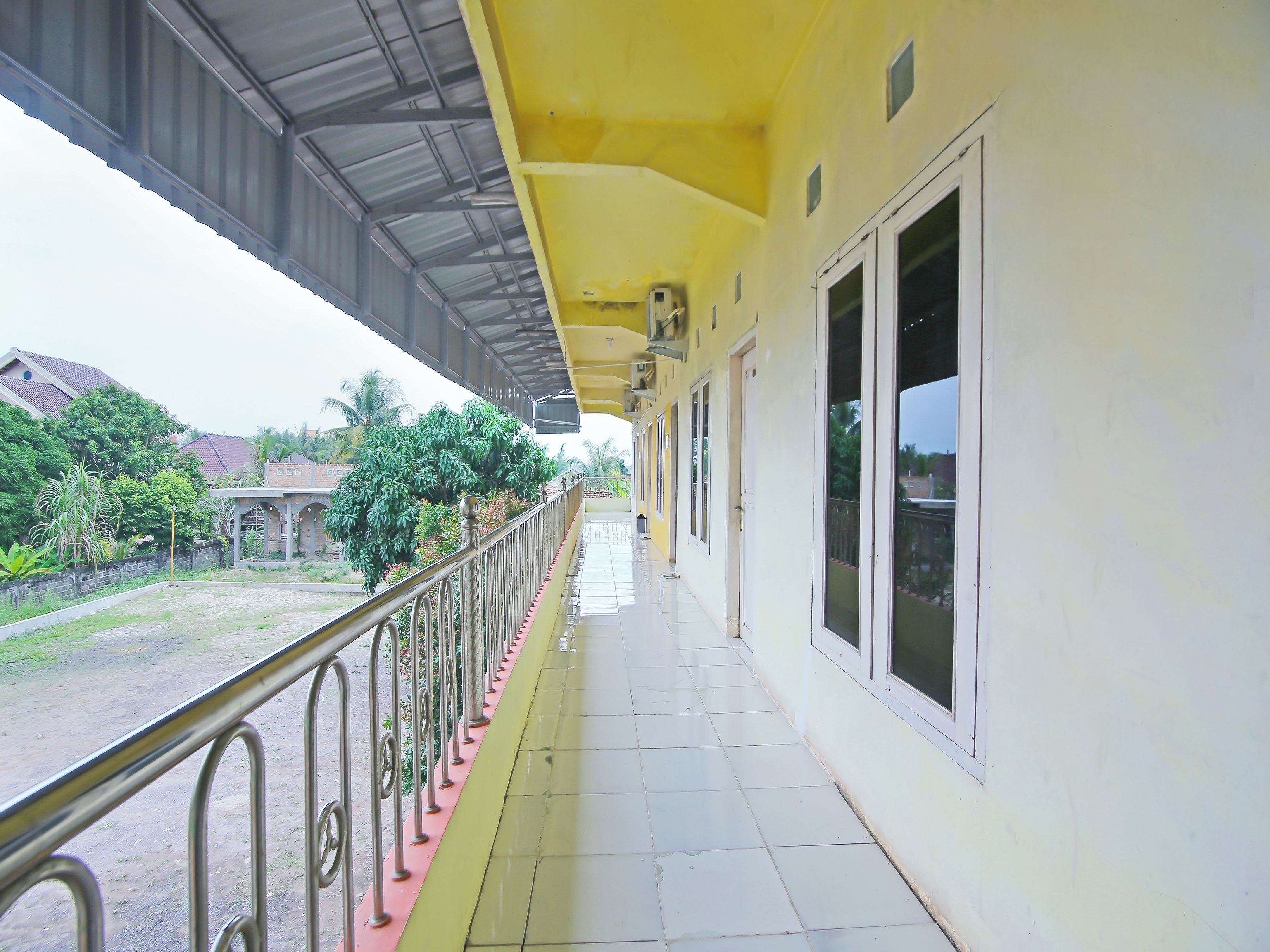 A corridor with a yellow exterior, metal railings, and large windows.