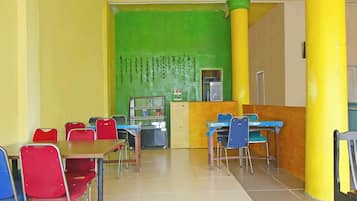 A cafeteria with tables and chairs, a vending machine, and a green wall with hanging plants.