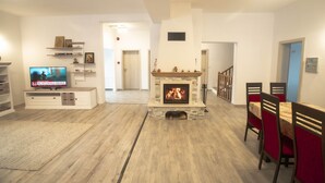 Een woonkamer met een open haard, een televisie en een eethoek met stoelen en een tafel.