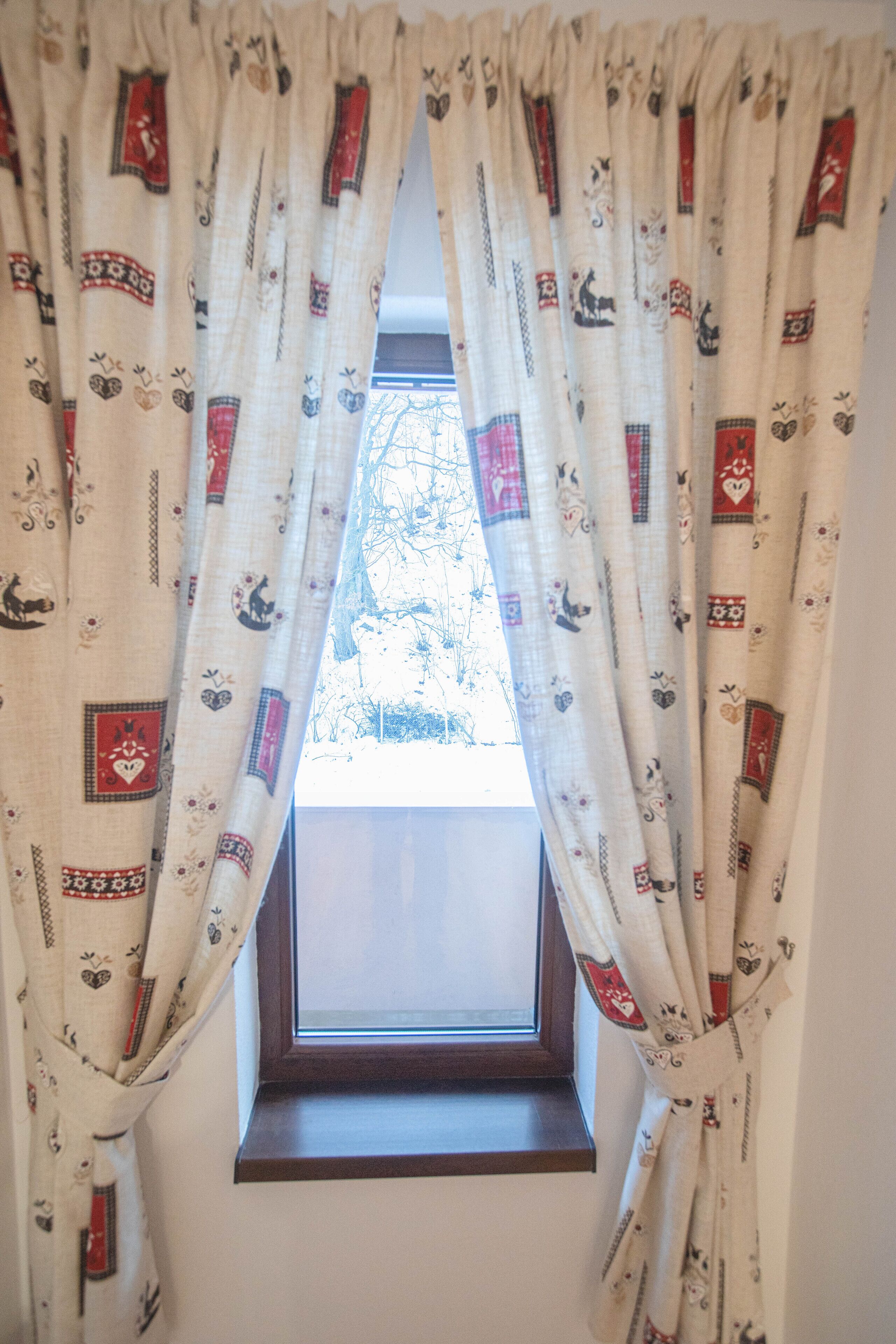 A window with a view of trees outside, covered by curtains with a pattern of animals and hearts.