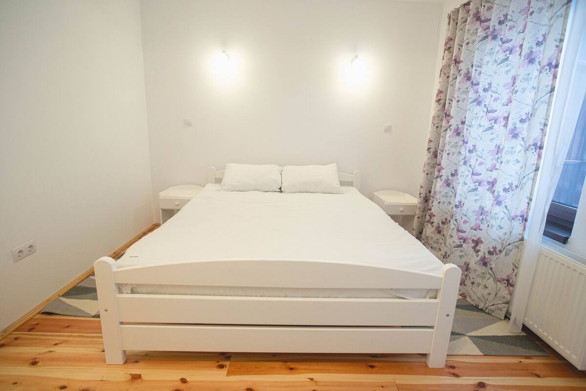 A bedroom with a single bed, a nightstand, a dresser, and a window with floral curtains.