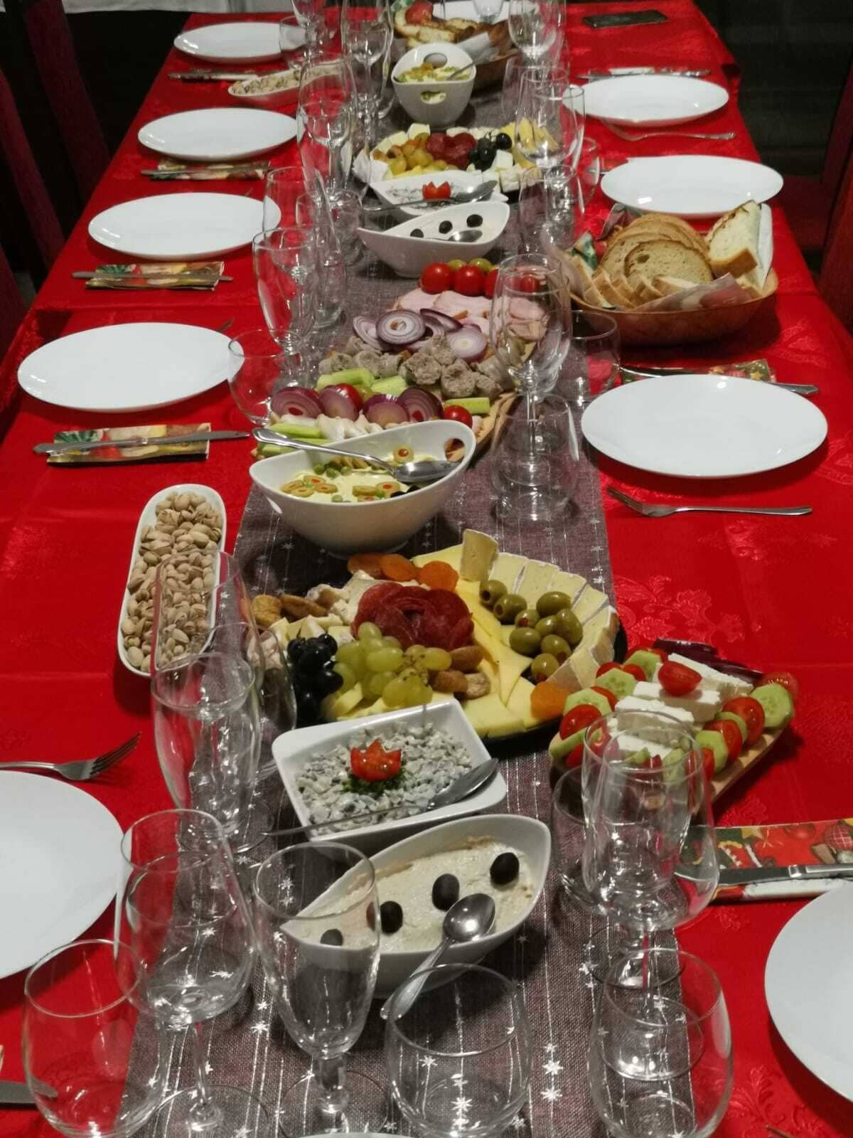 A long table set with various food items and wine glasses, covered with a red tablecloth.