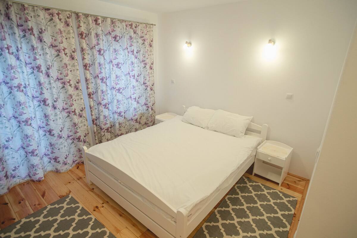 A bedroom with a bed, nightstands, a patterned rug, and a floral curtain.