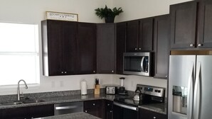 A modern kitchen with dark cabinets, stainless steel appliances, a granite countertop, and a bar stool. - Stunning New Home in Cape Coral Florida (Cape Coral)