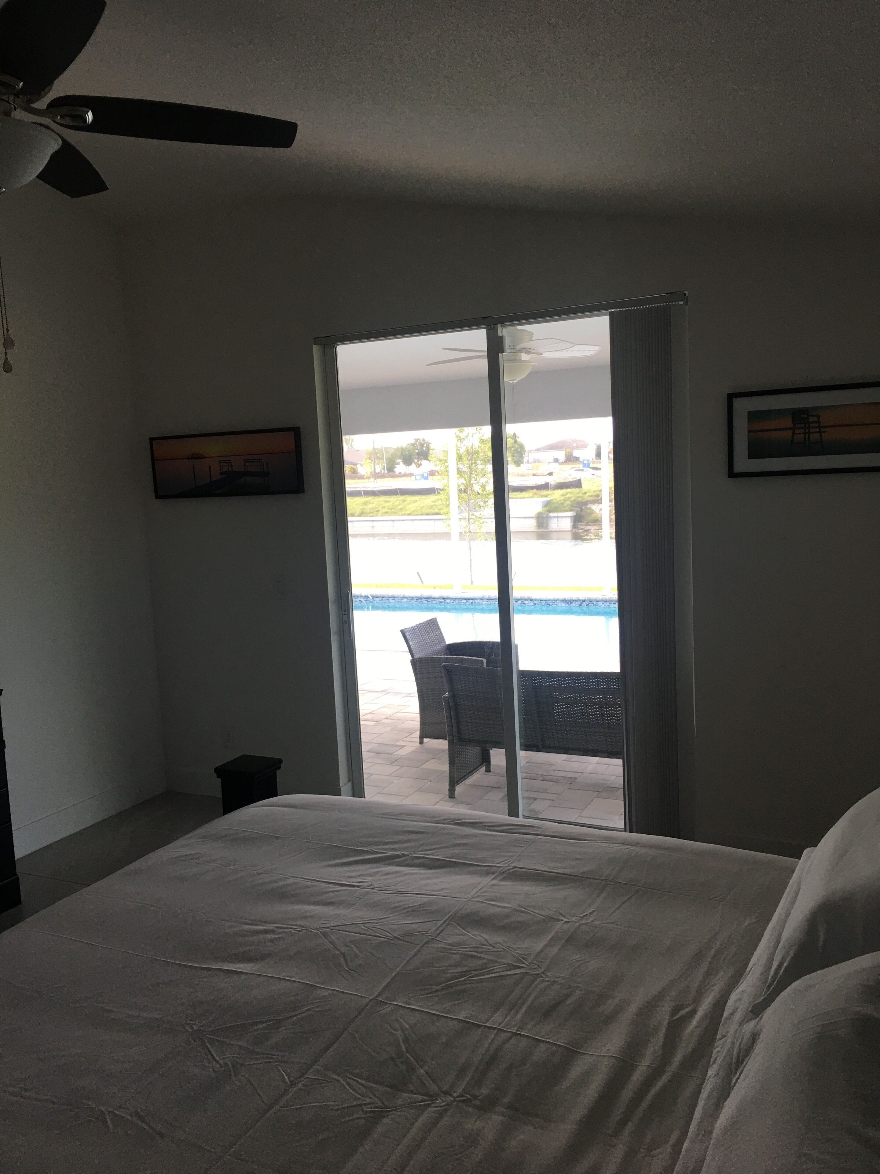 Une chambre d’hôtel avec un lit, un ventilateur de plafond, une vue sur une piscine et un espace extérieur aménagé accessible par une porte-fenêtre coulissante.