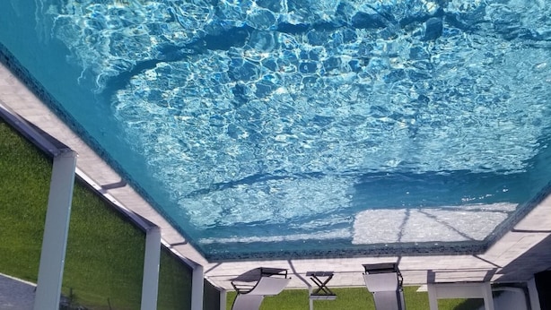 A clear view of a swimming pool with a glass ceiling, surrounded by a white structure with a grassy area in the background. - Stunning New Home in Cape Coral Florida (Cape Coral)