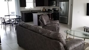 A modern living room with a leather sofa, a glass coffee table, and a dining area with chairs. - Stunning New Home in Cape Coral Florida (Cape Coral)