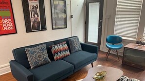 A living room with a dark blue sofa, patterned cushions, a small round table with a decorative item, a blue chair, and a vintage television. - Lower East side NYC in Old Bisbee (Bisbee)