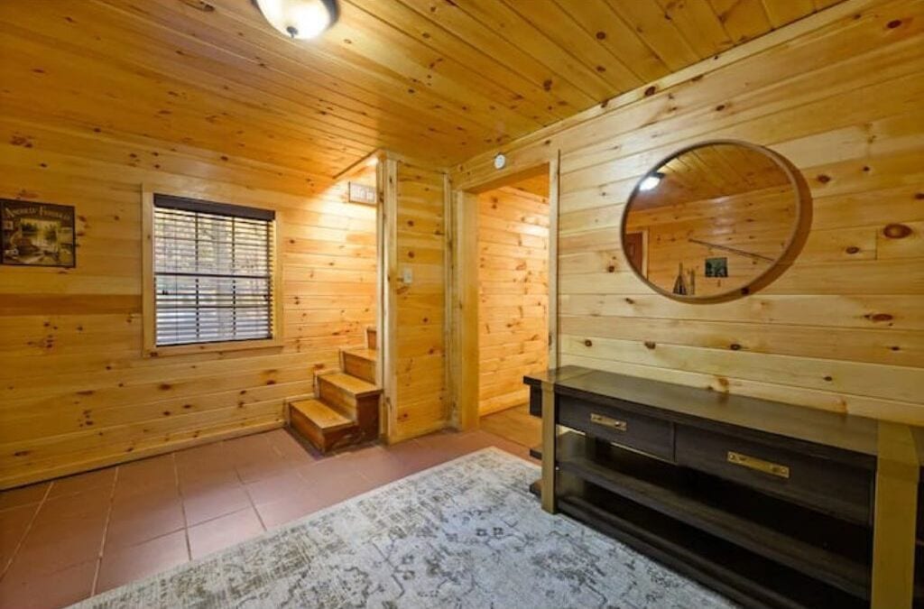 A wooden cabin interior with a staircase, a mirror, and a fireplace.