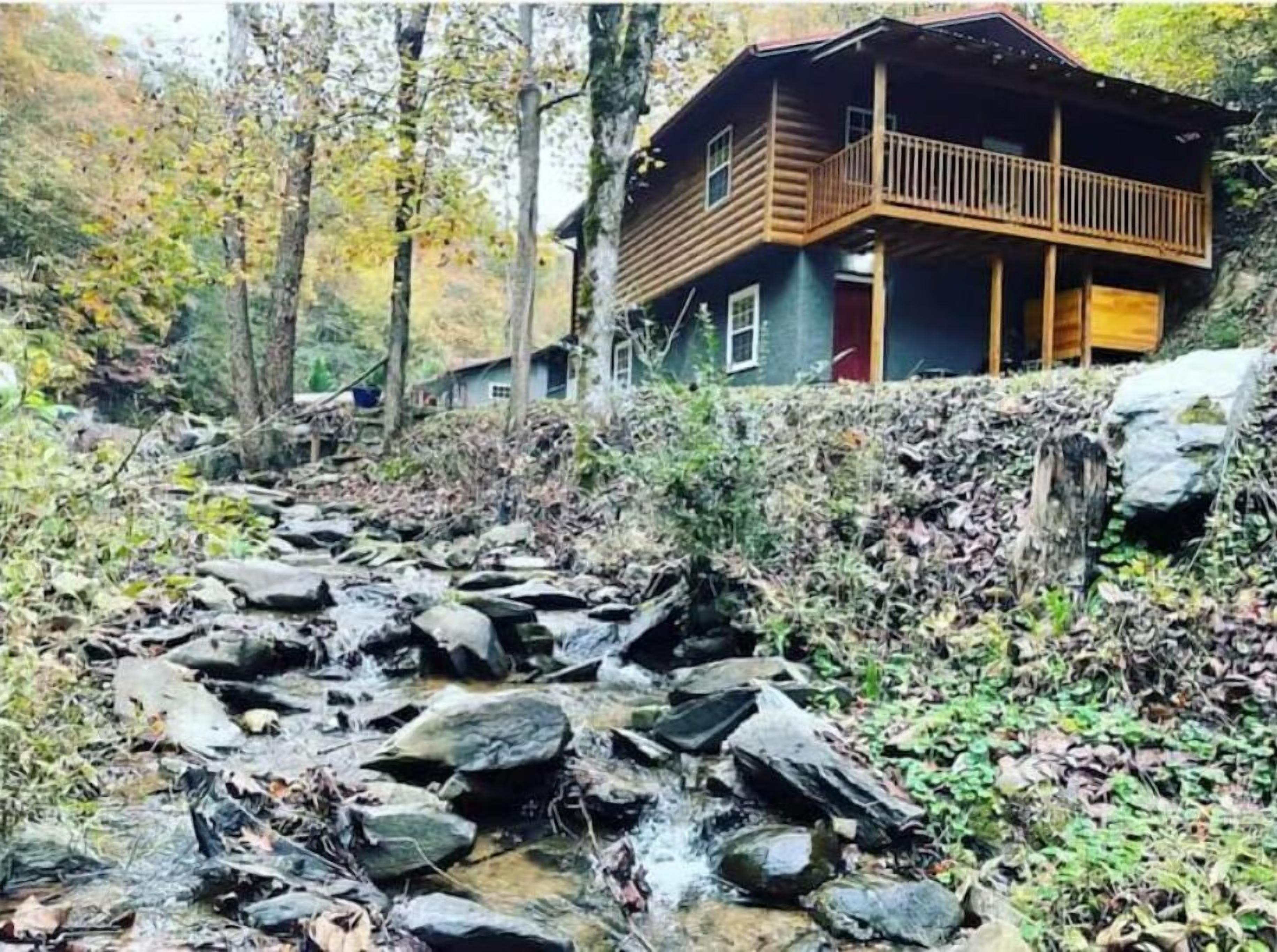 A cabin with a wooden deck and a stream in front.