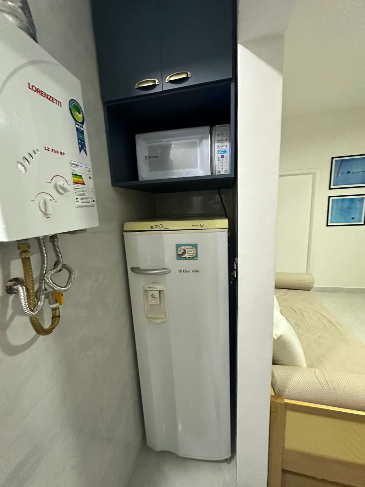 Habitación compacta con un calentador blanco, un refrigerador pequeño y un microondas en un estante.
