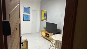 A room with a wooden door, a white door, a TV on a wooden stand, a small table with chairs, and two framed pictures on the wall. - Ap Copacabana 200m da praia - CP2 (Rio de Janeiro)