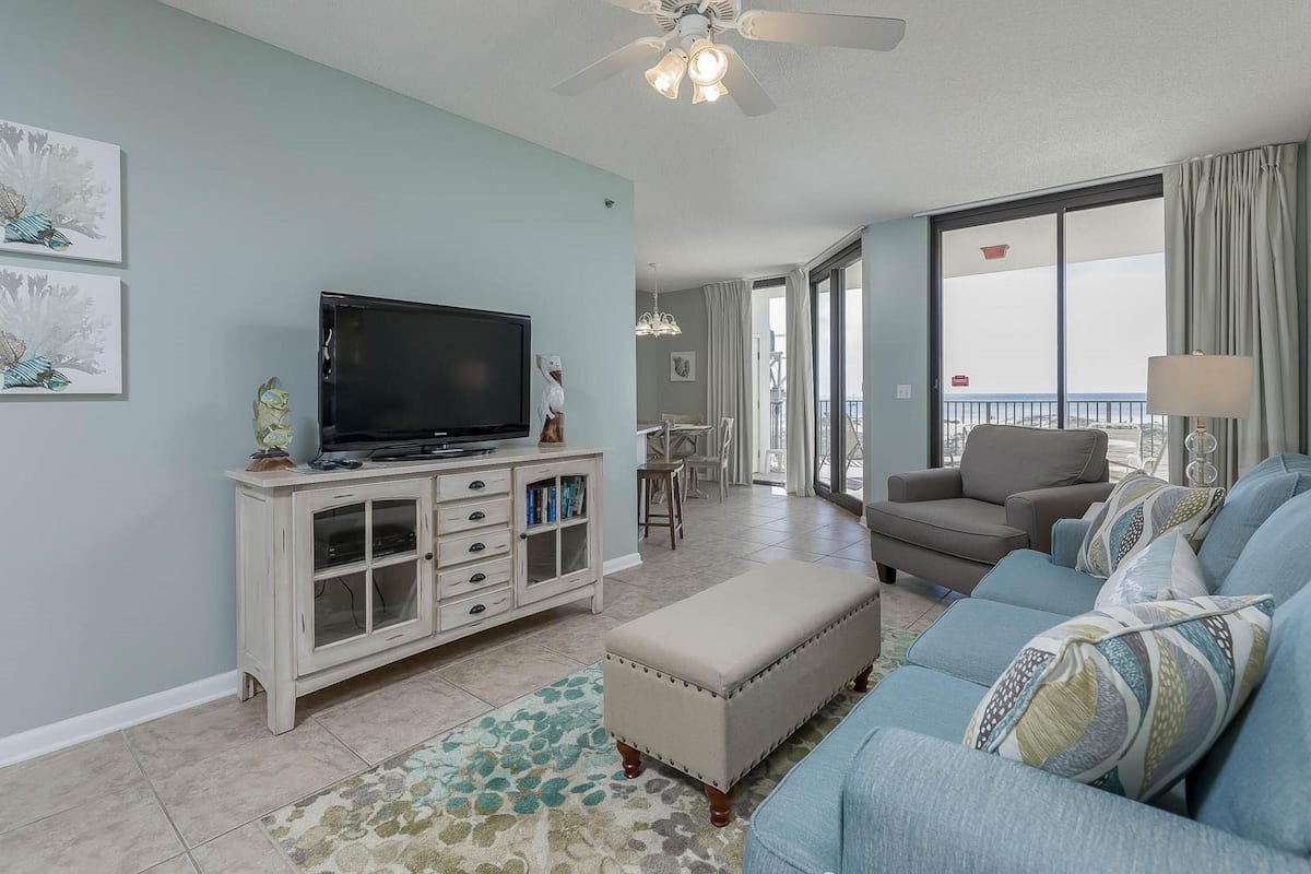 A living room with a TV, a sofa, a cabinet, and a balcony with a view.