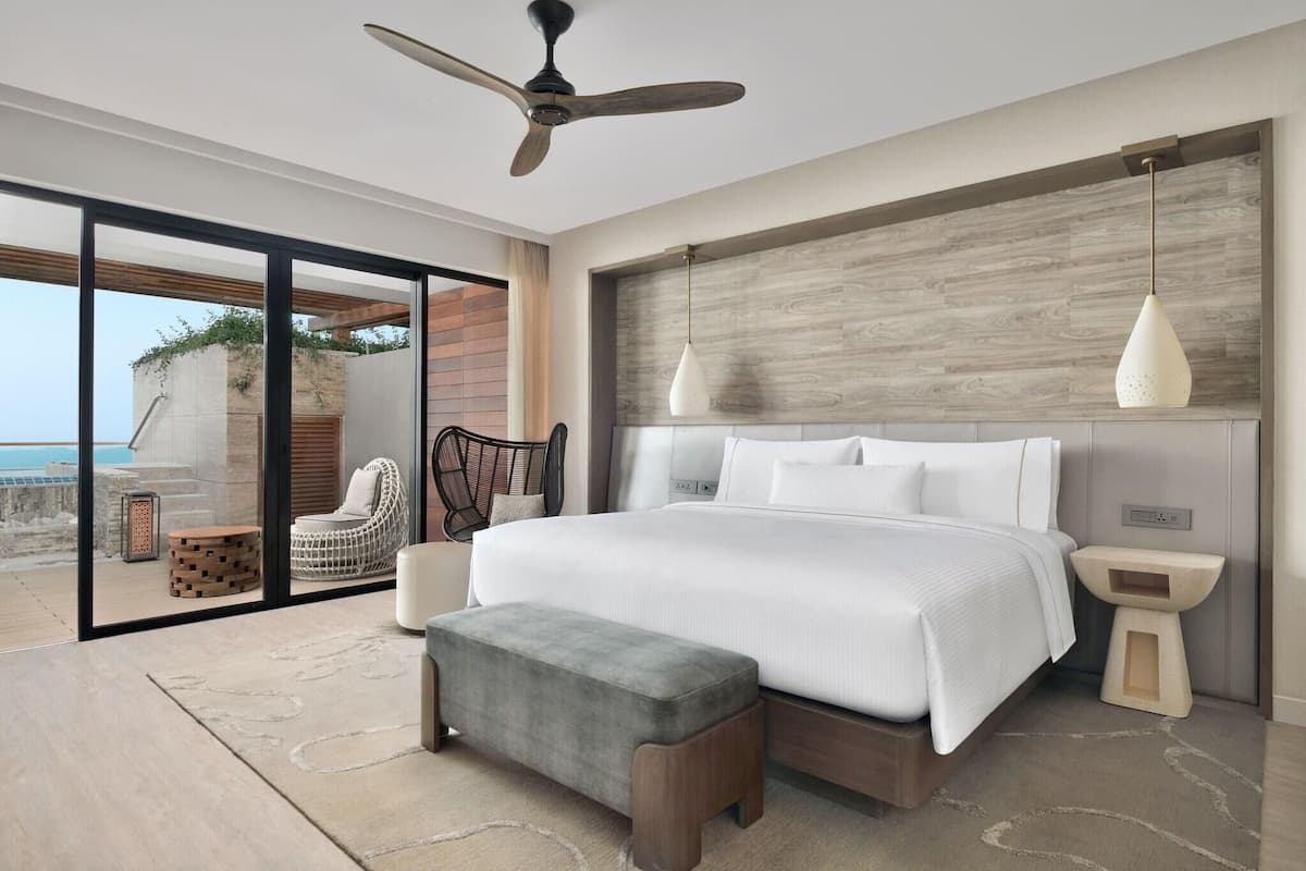 A modern bedroom with a large bed, a ceiling fan, and a view of the ocean.