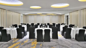 Un salón de conferencias con varias mesas, sillas negras y una alfombra estampada.