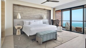 Un dormitorio moderno con una cama grande, ventilador de techo, vista al océano y balcón con mobiliario de mimbre.