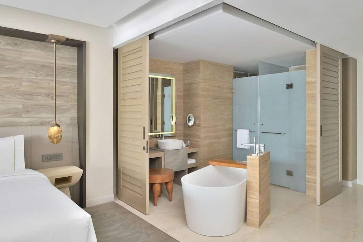A modern hotel room with a large bed, a round bathtub, a separate bathroom with a shower, and a wooden floor.