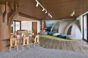 A modern children's playroom with a wooden floor, a table with chairs, a bookshelf with toys, and a large window. - The Westin Resort & Spa, Himalayas (Narendranagar)