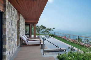 A modern outdoor area with a stone wall, wooden deck, lounge chairs, and a pool overlooking a scenic view. - The Westin Resort & Spa, Himalayas (Narendranagar)
