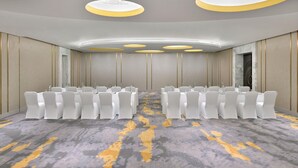 Un salón de conferencias con filas de sillas blancas, una alfombra estampada y un diseño moderno de techo.