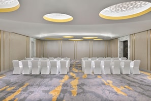 A conference room with rows of white chairs, a patterned carpet, and a modern ceiling design.