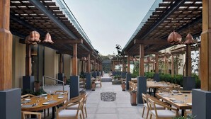 An outdoor dining area with wooden tables and chairs, surrounded by a covered walkway with hanging pendant lights. - The Westin Resort & Spa, Himalayas (Narendranagar)