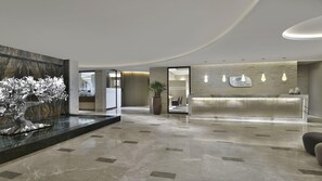 Eine moderne Lobby mit einer Rezeption, einer dekorativen Baumskulptur und einer großen Pflanze in einem Topf.