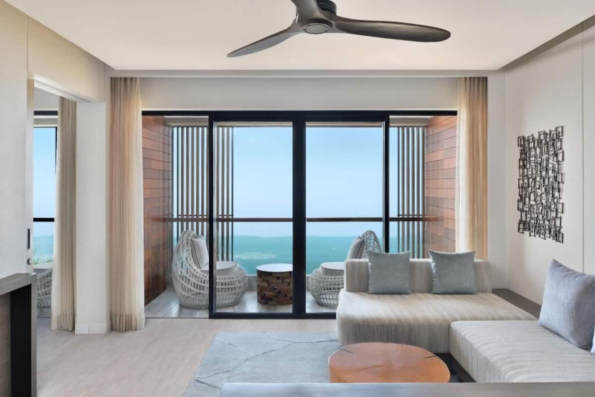 A modern living room with a large window, a ceiling fan, and a view of the ocean.