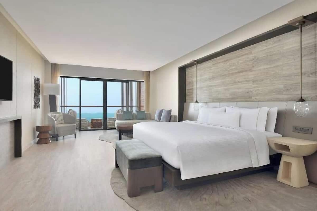 A modern hotel room with a large bed, a seating area with a view, and a flat-screen TV.