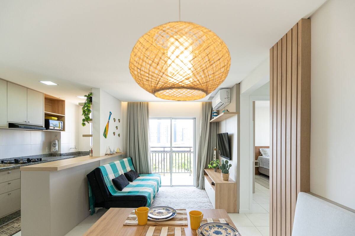 A modern kitchen with a built-in stove, a dining area with a table and chairs, a sofa, and a large window with curtains.