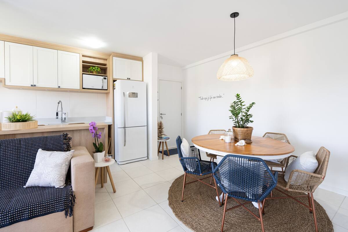A modern kitchen with white cabinets, a refrigerator, and a dining area with a round wooden table and blue chairs.