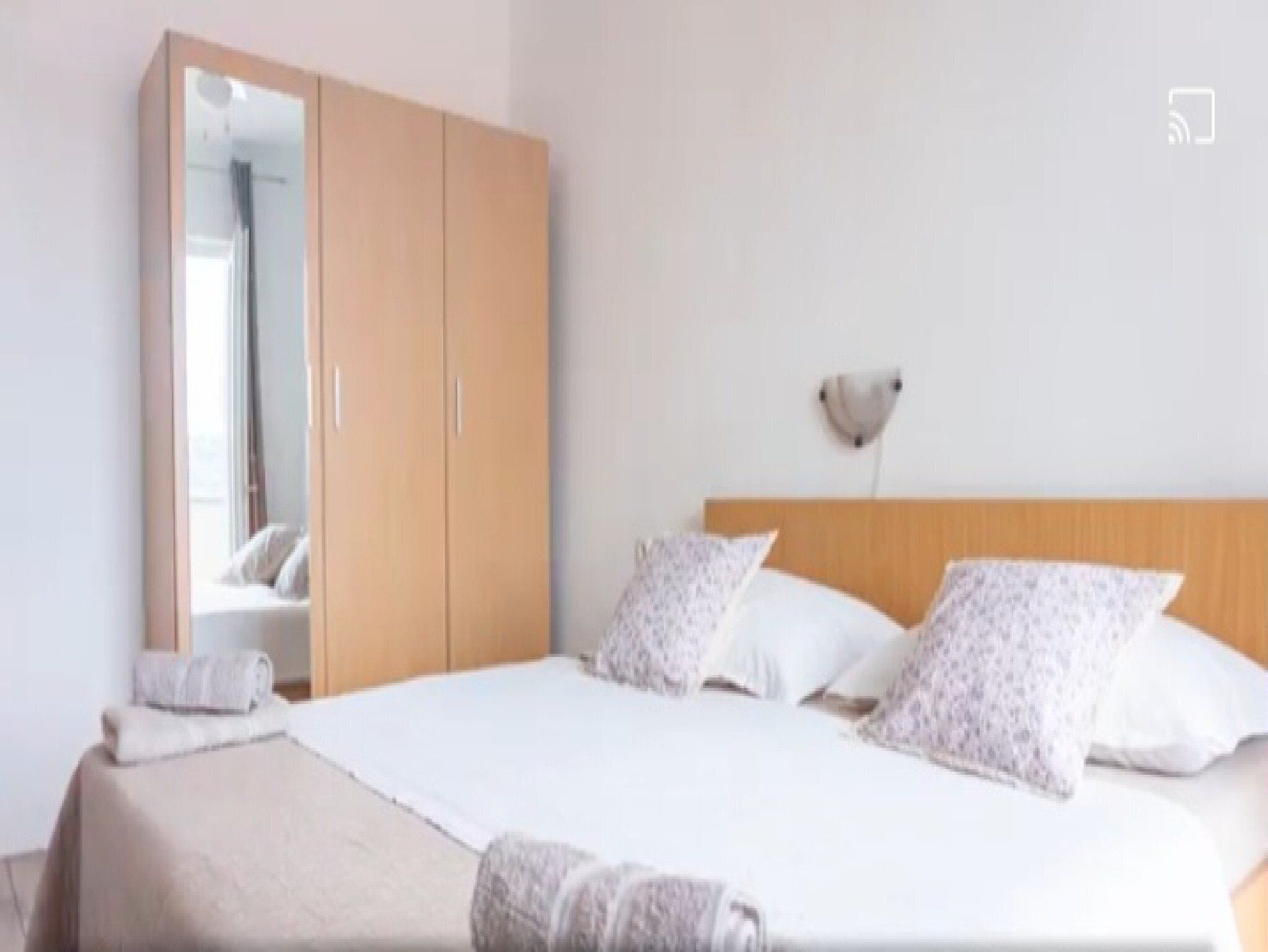 Une chambre à coucher avec un lit, des oreillers, une table de chevet, une armoire et une lampe fixée au mur.