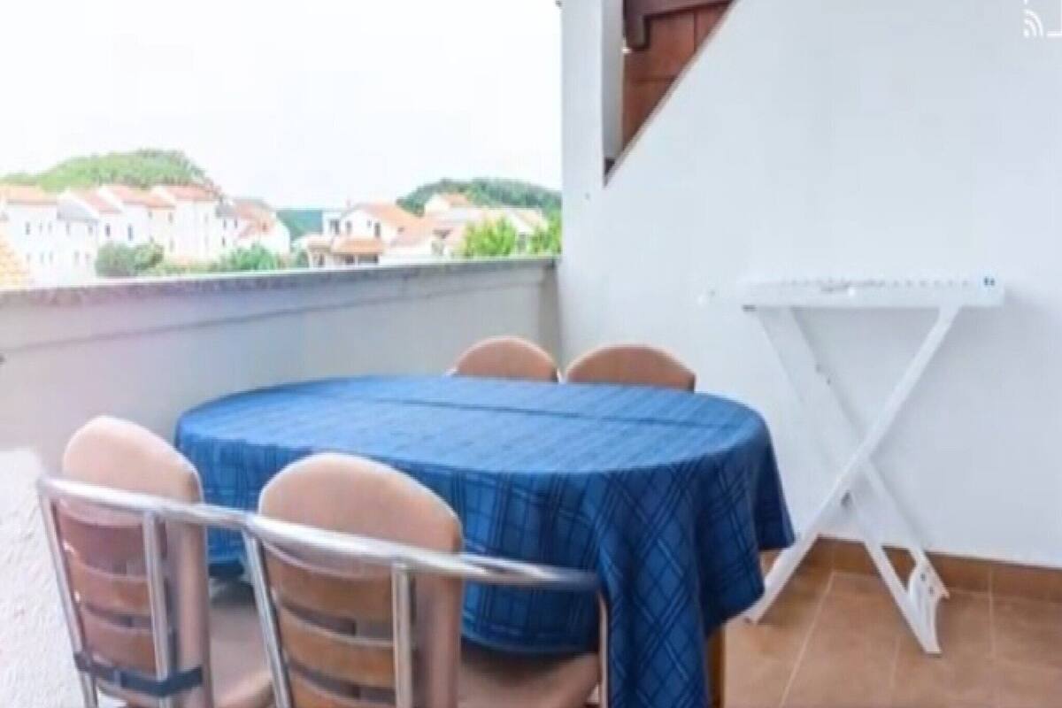 A balcony with a round table and chairs, a white folding table, and a view of buildings in the distance.