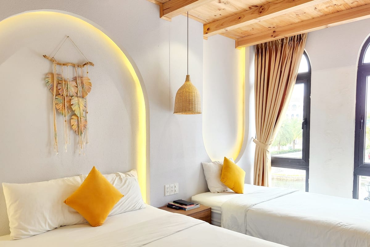A bedroom with two beds, a dreamcatcher, a hanging light, and a window with curtains.