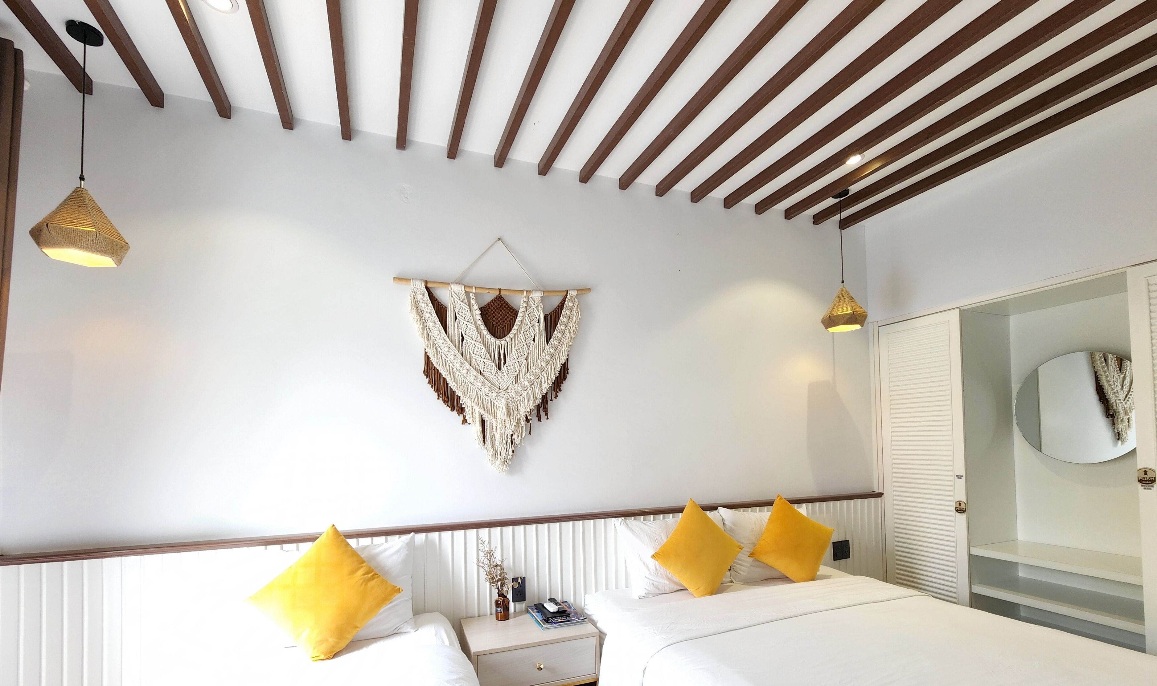 A bedroom with a bed, bedside tables, a macrame wall hanging, and a ceiling with wooden beams.