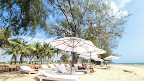 A beach with lounge chairs and umbrellas, palm trees, and a clear sky. - Riverside Mini Hotel Grand World (Phu Quoc)