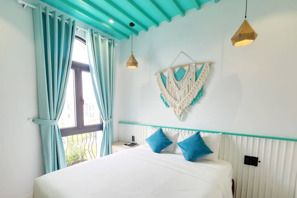 A bedroom with a bed, teal curtains, a macrame wall hanging, and pendant lights.