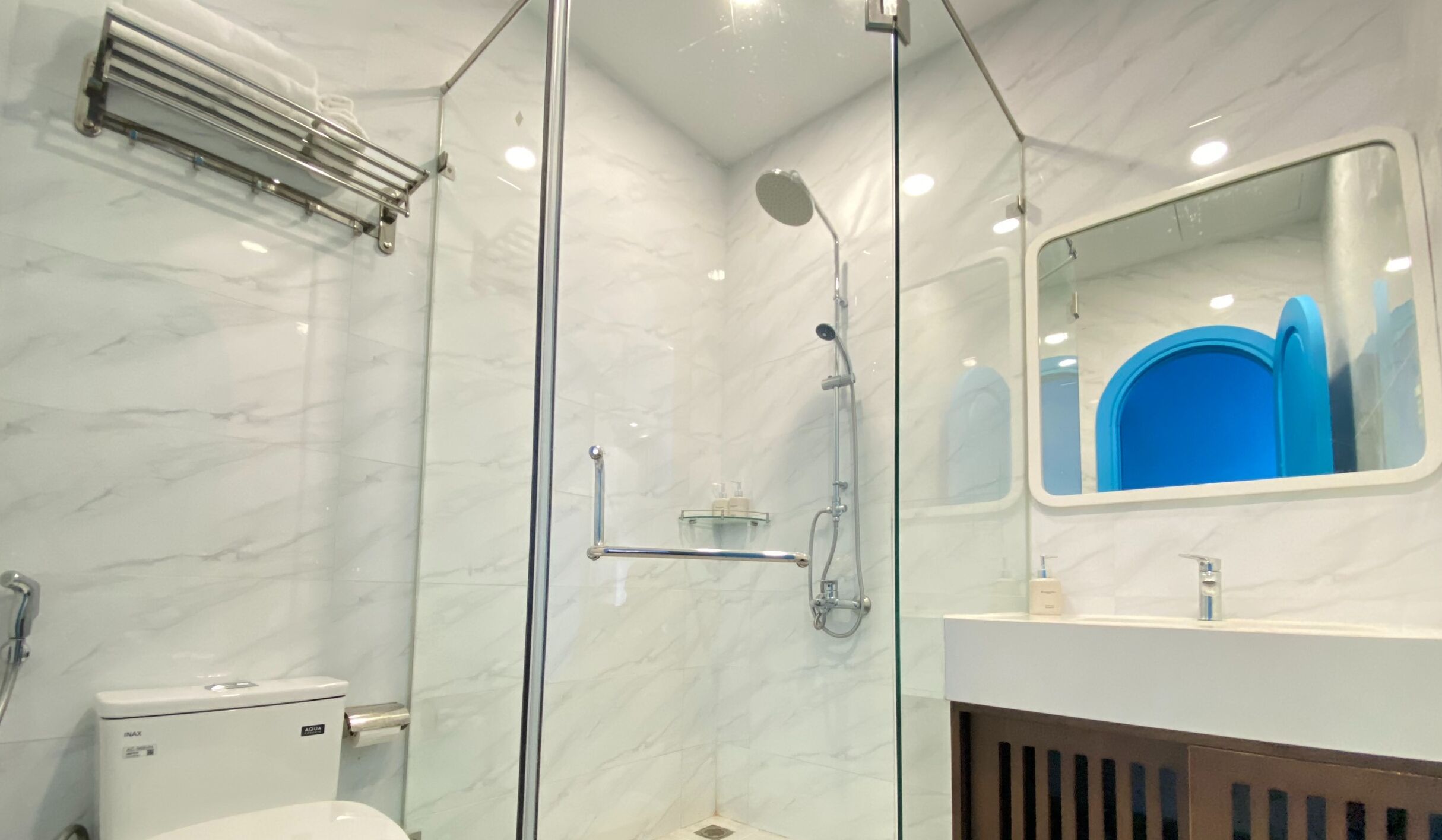A modern bathroom with a glass-enclosed shower, a toilet, and a sink with a mirror above it.