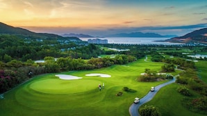 A golf course with bunkers, a water body, and distant mountains. - Riverside Mini Hotel Grand World (Phu Quoc)