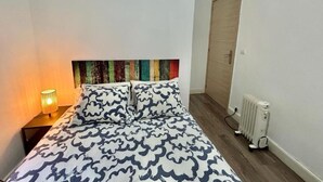 Una cama individual con ropa de cama estampada, una lámpara de noche, un radiador y una puerta de madera.